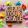 Sign that says CLEAR YOUR SPACE surrounded by colored crumbled paper on hardwood