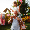 Grandpa with child on his shoulders both carrying US flags in backyard