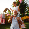 4th of July Grandpa with child on his shoulders both carrying US flags in backyard