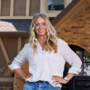 blonde woman wearing a white shirt and blue jeans standing in front of a house
