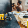 Close up of yellow drill on table with blurred male in background doing home renovation