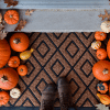 Bird's eye view of brown welcome mat surrounded by mini pumpkins with brown boots walking over it
