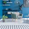 Bright blue room with vertical stripe area rug and simple grey chair with some wall shelving and steel art pieces