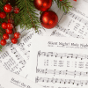 pages of sheet music spread across a table with red ornaments placed above
