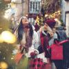 two women holding shopping bags walking through a holiday market