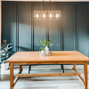 Heather Campbell Brown kitchen wooden table with floral centerpiece, four hanging lights and a green painted wall