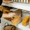 Hand reaching into organize pantry, organized cereal in clear boxes.