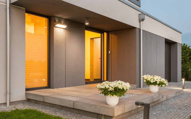 exterior of home with custom outdoor lighting. White roses in white pots on tiled walk out veranda