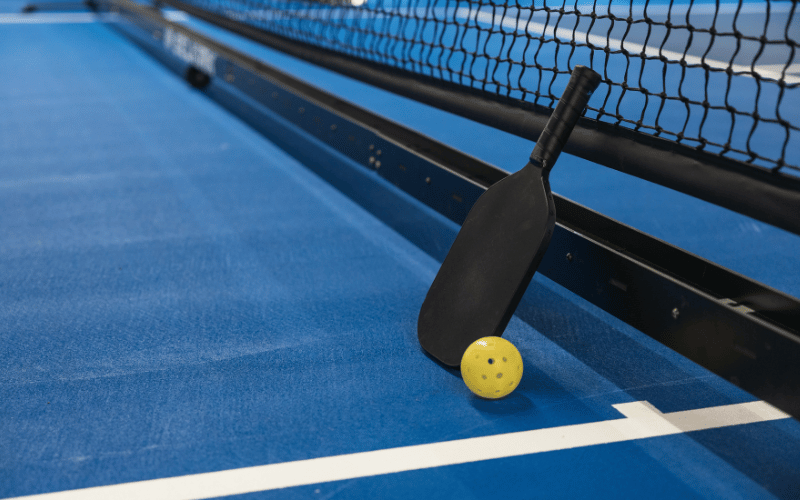 A pickleball and racket placed on the ground of a court 