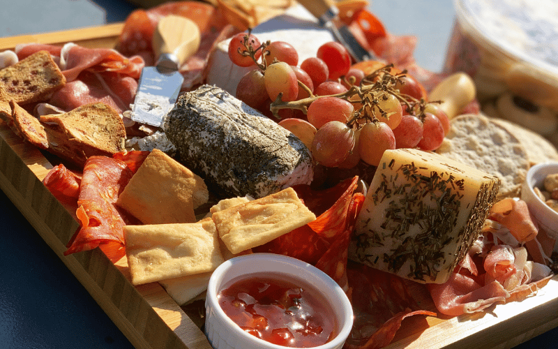A cheese plate filled with crackers, cheese, cured meats, and jam