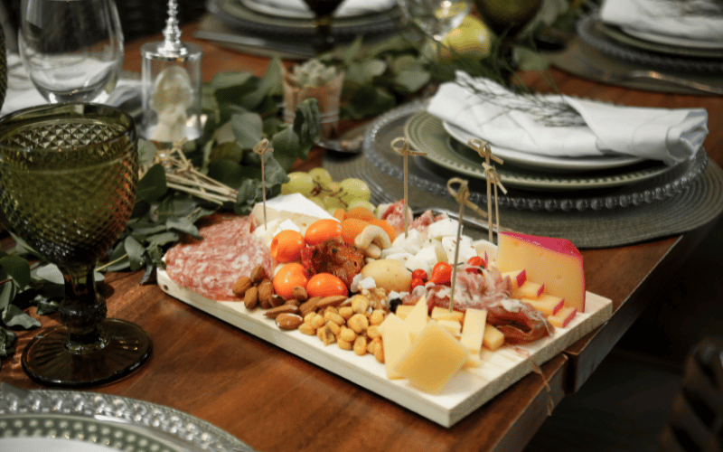 A dinner table with a plates and a board full of cheese, grapes, and meats 