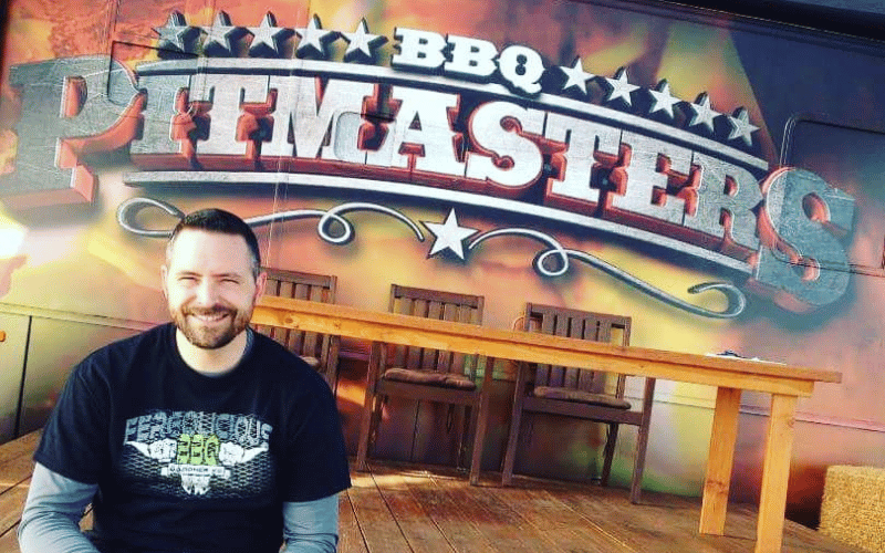 a man smiling standing in front of a barbecue poster 