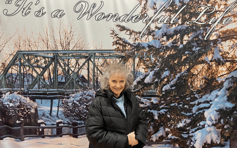 woman with a black jacket standing in front of trees covered with snow