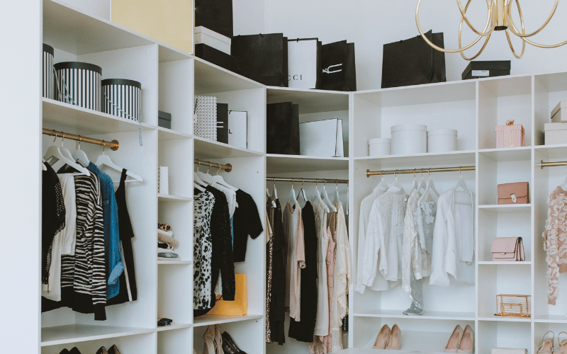a walk in closet with black and white shoe boxes above and folded stacks of clothes on the shelf