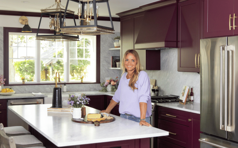 blonde woman standing in a large open kitchen with purple accents 