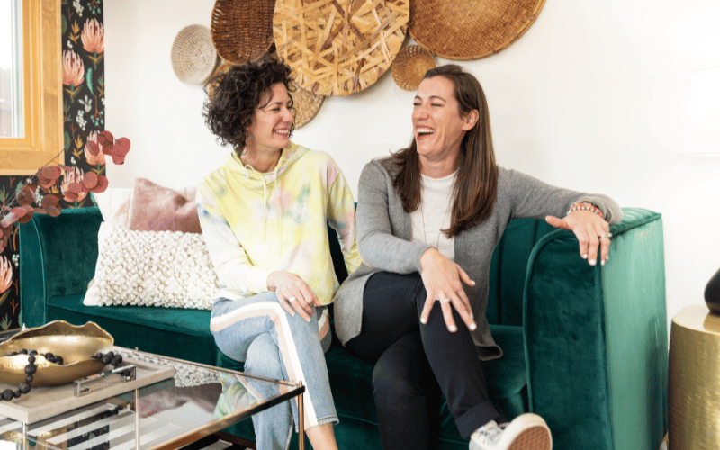 two women smiling and sitting on a couch 