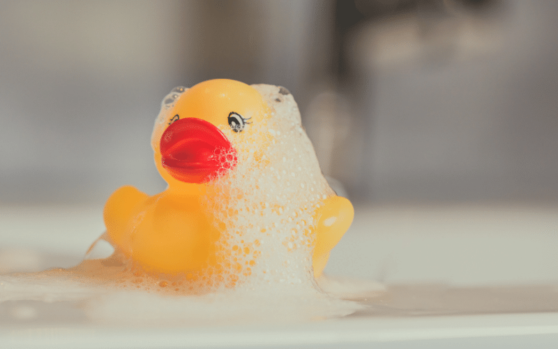 yellow rubber duck covered in bubbles in sink