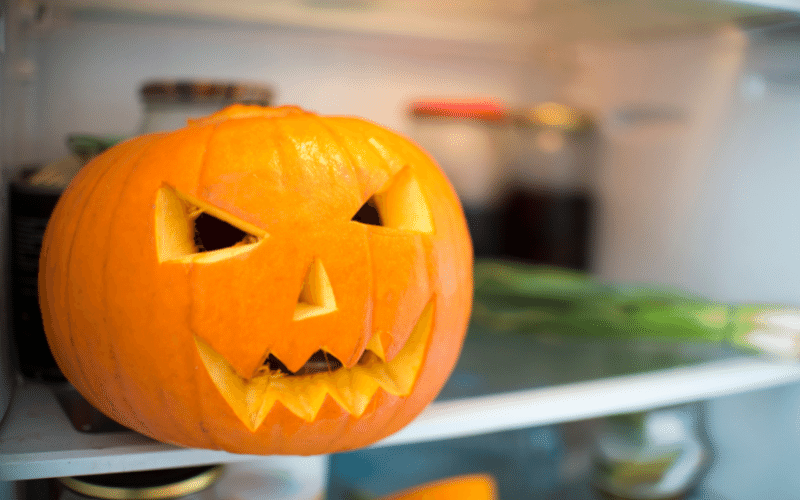 Carved jack o lantern on fridge shelf next to green onions blurry 