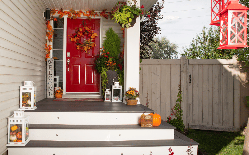 Fall decorated front porch with bright red painted front door and welcome vertical block sign