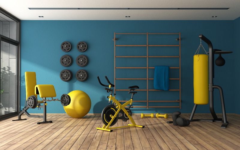 Bright yellow exercise equipment and pilates ball and punching bag in home gym with bright blue wall and hardwood plank floor