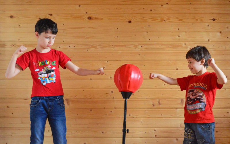 Two young boys wearing red tshirts exercising punching at punching ball having fun 