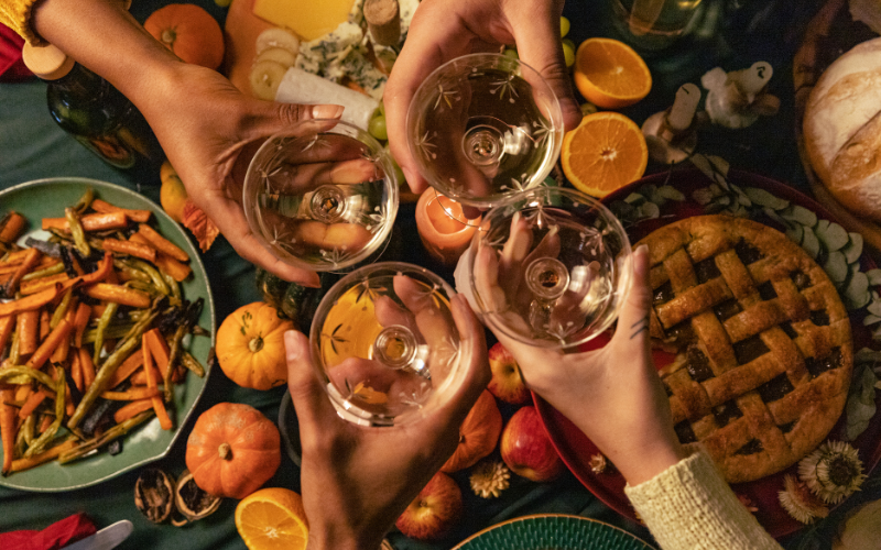 four friends toasting white wine over Thanksgiving dinner 