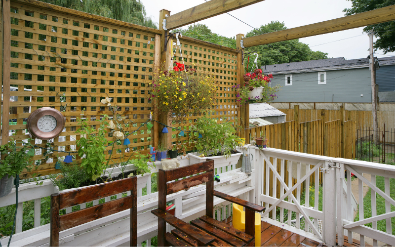 Small backyard porch with dark wood chairs and hanging plants beside white gate