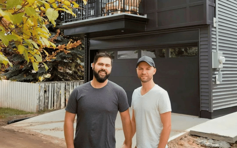 Stephen & Branden The Visionary Husbands standing in front of modern black stacked renovated home