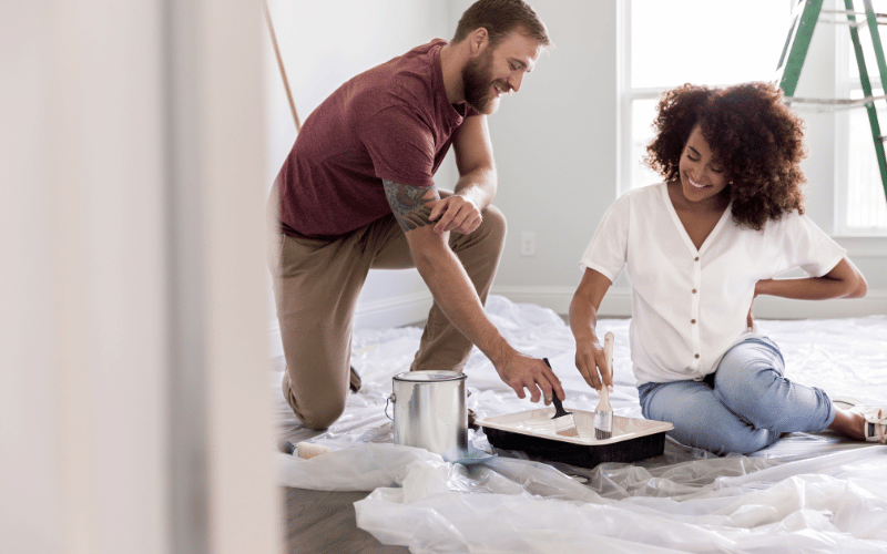 Couple crouched over drop sheet painting their room with white paint