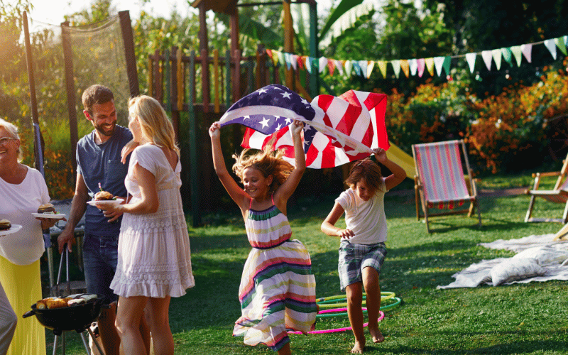 Kids running with American flag in the backyard on the grass during a family barbecue