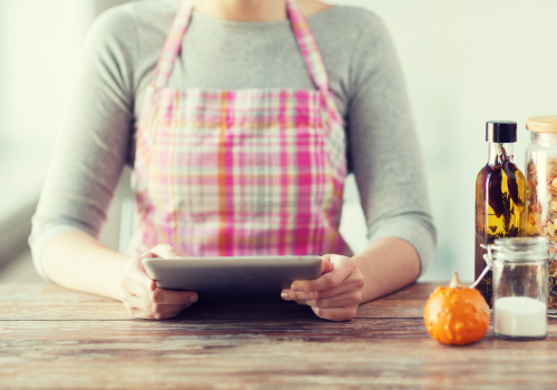 Woman wearing pink plaid apron reads recipe on ipad with ingredients on counter