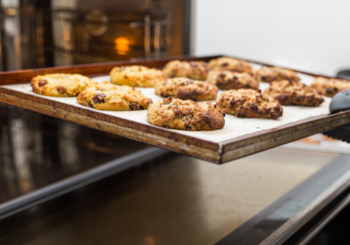 Old rusty baking sheet with parchment paper and 12 medium sized cookies coming out of oven