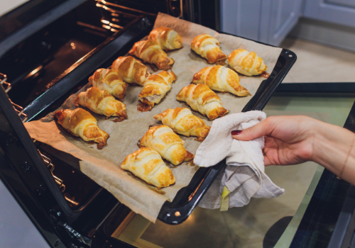 New nonstick dark colored baking tray lined with parchment paper and 14 fresh croissants coming out of oven