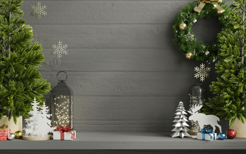 Front mantle dark grey with mini pine trees flanking miniature holiday decorations. White Christmas tree, mini red and white gift, lantern. On right, silver tree, white reindeer and mini blue and white gift