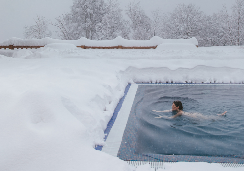 Woman swimming in in-ground pool in winter with snow surrounding pool