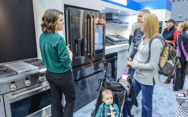 Couple shopping for full size stainless appliance at the home show being assisted by young woman in teal shirt