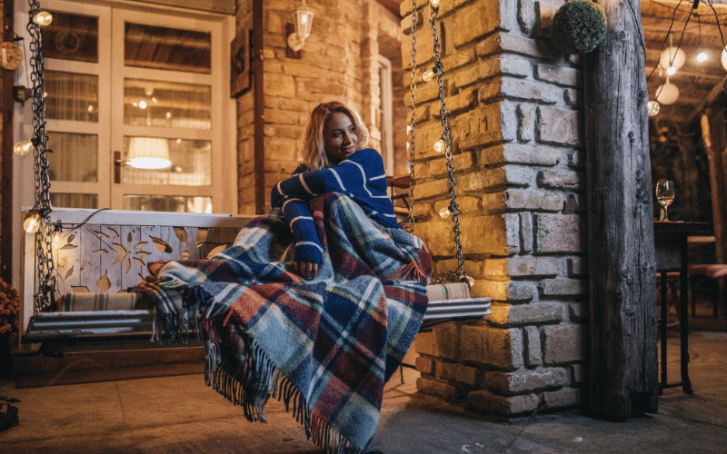 Blonde woman sitting on porch swing under plaid blue blanket at night