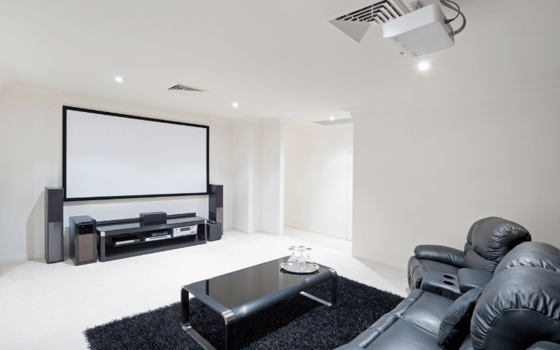 White room interior with wall mount cinema screen and entertainment console and black leather furniture