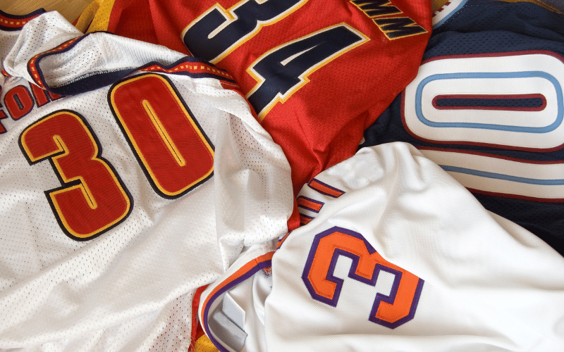 Pile of football jerseys. White jersey with red 30, white jersey with orange 3, red jersey with black 34 and black jersey with grey 10