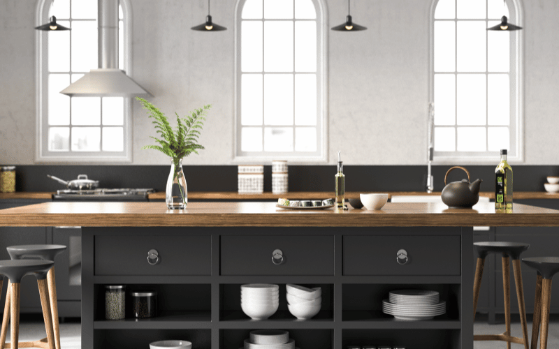 Modern Kitchen with black bar island and dark wooden countertop, bar stools, hanging black pot lights and a leafy plant on the bar