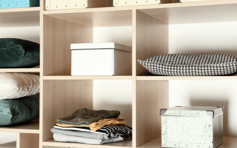 Organized wall shelving unit with boxes, blankets, pillows and clothing inside the different shelves