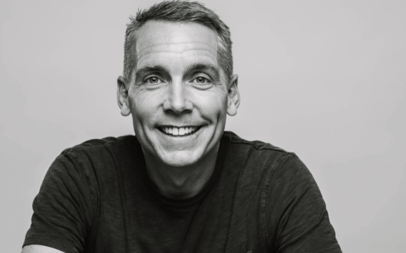 Black and white photo of Clint Harp posing and smiling wearing black tshirt