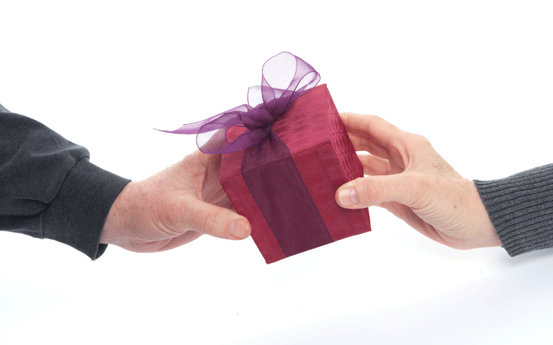 Close up of hands handing small red gift box to other hand