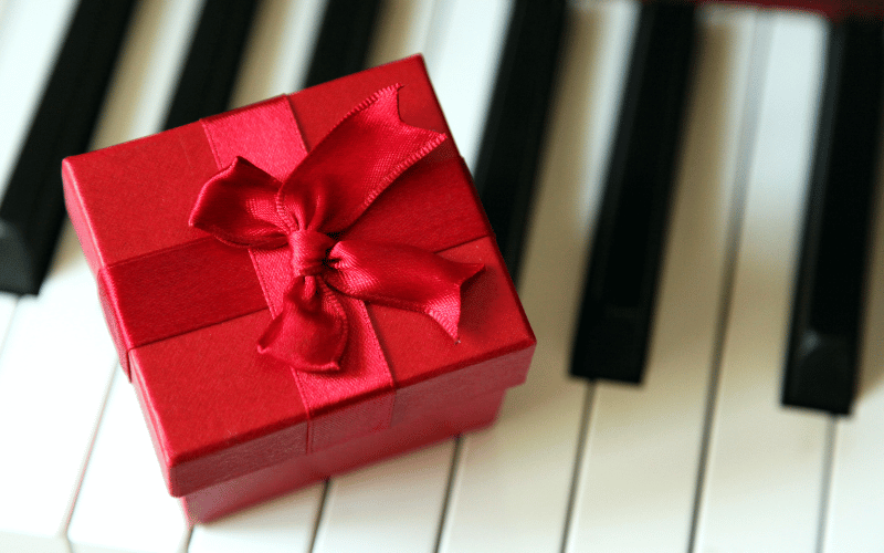 Red high end gift box with bow sitting on top of Piano