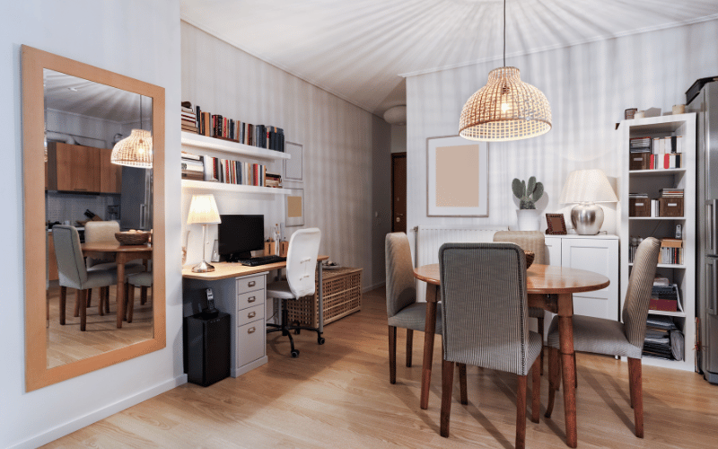 Small kitchen-office workspace with full length wall mirror, ceiling hanging light grey chairs, brown table and white walls