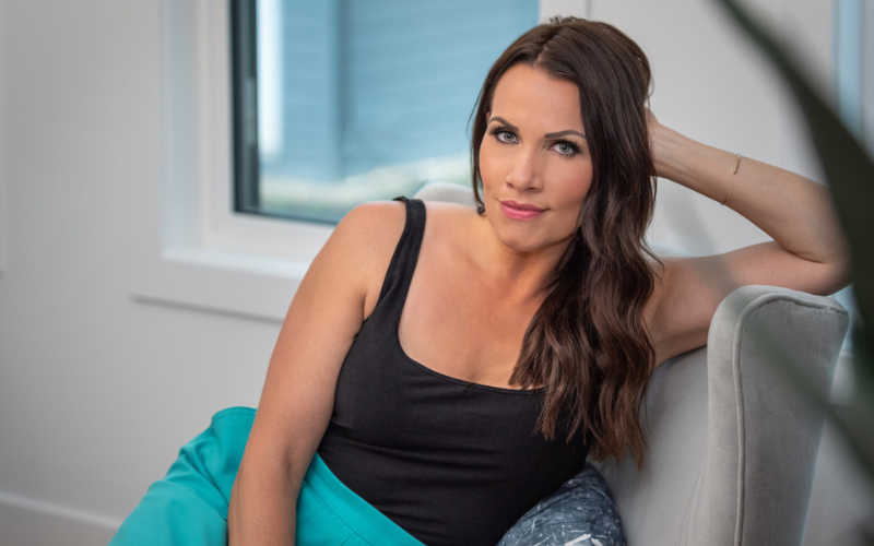 Jennifer Hughes leaning into grey armchair with left hand against ear wearing black tank top and turquoise bottoms