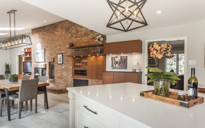 Jennifer Woch design kitchen with geometric metallic ceiling light, white island with centrepiece looking onto exposed brick living room wall