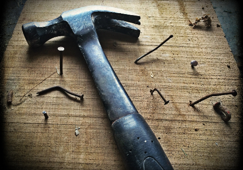 Black hammer laying on piece of wood with many bent and broken nails