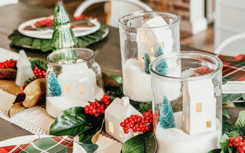a table laid with holiday decor surrounding glass jars 